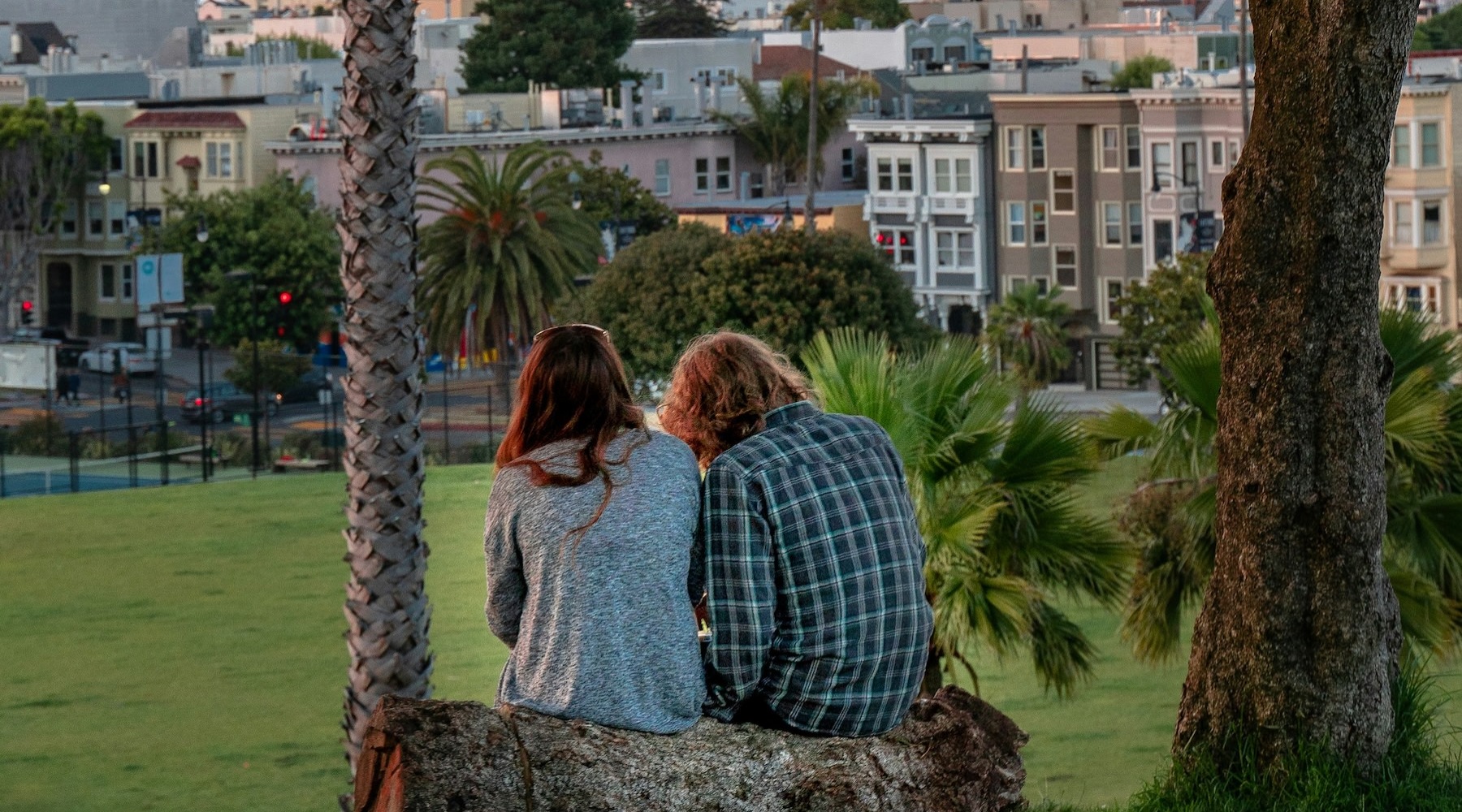 a couple sitting on a rock looking at a city